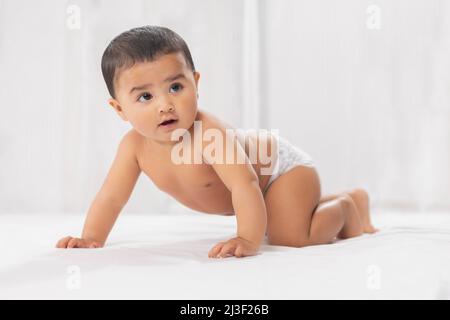 Cute baby in diaper crawling on bed Stock Photo