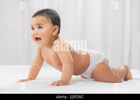 Cute baby in diaper crawling on bed Stock Photo