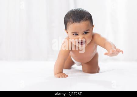 Cute baby in diaper crawling on bed Stock Photo