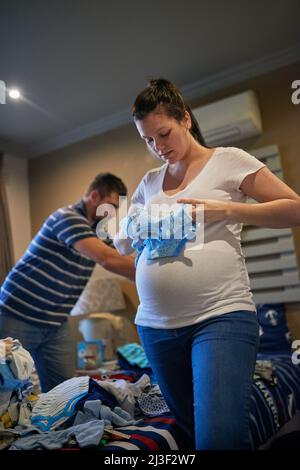 Sorting out babys wardrobe. Shot of a loving pregnant couple folding baby clothes together at home. Stock Photo