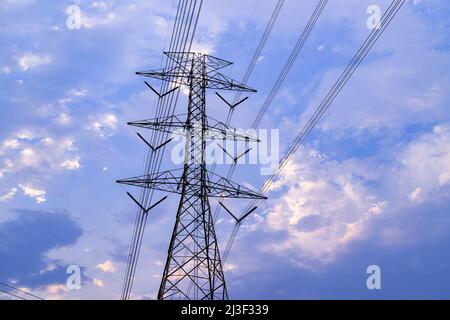 Evening clouds moving behind power line tower during sunset Stock Photo