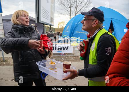 Medyka, Poland. 6th Apr, 2022. An Italian volunteer at Siobhan's Trust kitchen won't let anyone pass without eating French friends and having a hot drink to warm the body and soul at Medyka humanitarian border camp in Poland. Here he makes a Ukrainian refugee woman with a little dog in red sweater laugh, when she was looking very sad and tired since crossing the border. This Scottish-based organization supplying the food is founded for 'The advancement of citizenship or community development'' (according to their website.) They are supplying enough food and drink and smiles to sustain Stock Photo