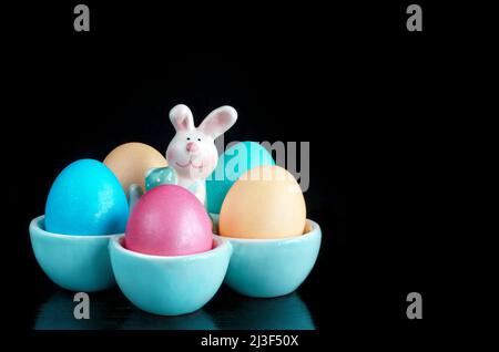 Colorful Easter eggs in a stand with a funny rabbit on a black background. Lots of space for text. Selective focus, the concept of Easter Stock Photo