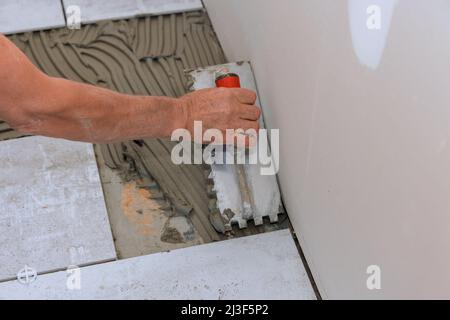 Master puts adhesive base over floor for ceramic tile Stock Photo