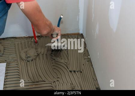 Applying adhesive with mason trowel over floor for ceramic tile Stock Photo