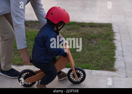 Father teaching his toddler boy to ride a balance bike for the