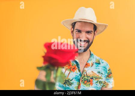 happy good-looking Latin American man with a white hat holding a red rose orange background studio shot medium closeup well-being concept. High quality photo Stock Photo