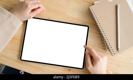 Overhead, Female hands touching or using digital tablet on wooden table. Tablet white screen mockup. Stock Photo