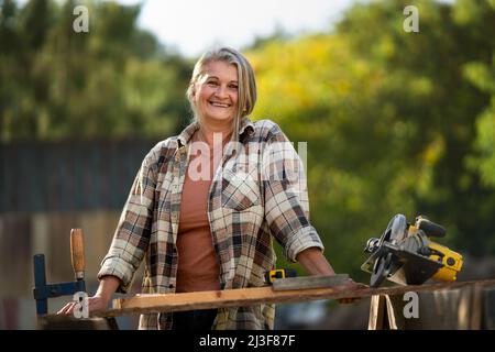 Happy handy female carpenter working in carpentry diy workshop outdoors with circular saw Stock Photo