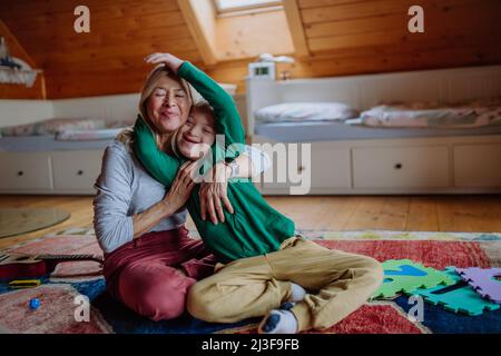 Happy boy with Down syndrome sitting on floor and hugging with his grandmother at home. Stock Photo