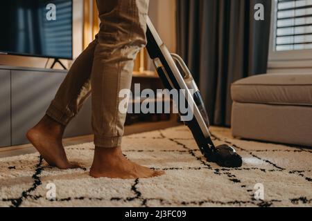 Lowsection of man hoovering carpet with vacuum cleaner in living room Stock Photo