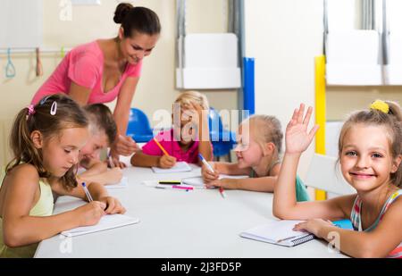 children making writing exercises with help of teacher in class Stock Photo