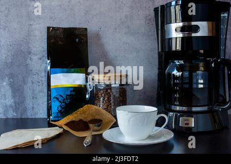 Coffee machine, a cup, a jar full of coffee beans and a spoon of  filter coffee. a hand pouring filter coffee Stock Photo