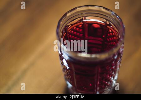 Close up tincture of red color in a crystal glass stands on a wooden table Stock Photo