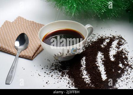 photo studio of black coffee in a cup with coarse coffee grounds and a brown cloth on white background and green plant Stock Photo