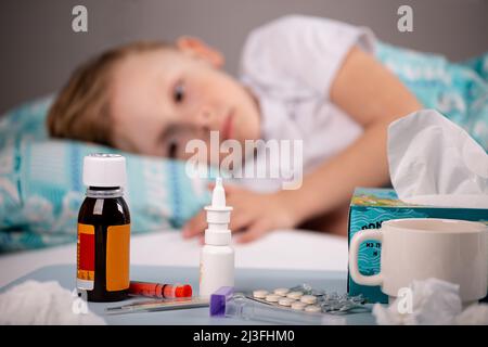 Medications, a thermometer, pills against the background of a sick child lying in bed, Focus on a table with medicines. Stock Photo