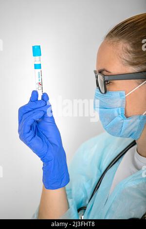 a girl, a medical worker, examines a test tube with a positive test result for covid-19 Stock Photo