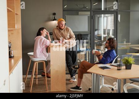 Group of young office colleagues laughing and chatting while drinking coffee and enjoying break together Stock Photo