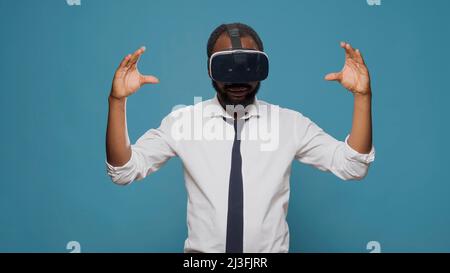 Male freelancer using vr glasses with futuristic vision in studio, working on innovative simulator. Young adult enjoying virtual reality goggles with 3d visual simulation, electronic headset. Stock Photo