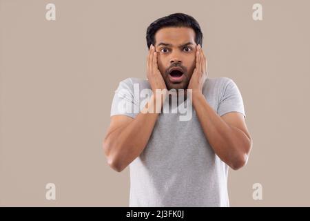 Portrait of a surprised young man with mouth opened and hands on cheek Stock Photo