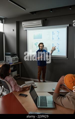 Young mixed race analyst pointing at projection screen while presenting statistics at staff meeting Stock Photo