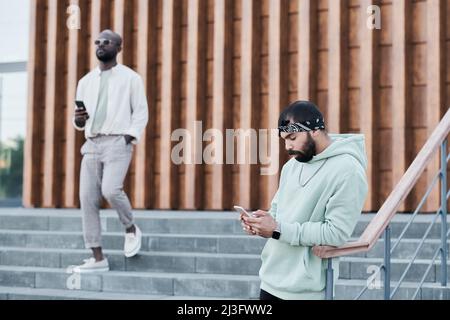 Middle eastern guy reading messenger chat while black man using phone on move Stock Photo