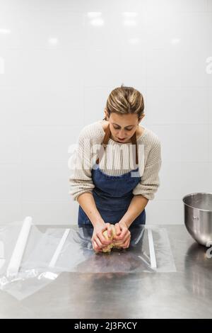 Female baker kneading dough on table in bakery Stock Photo