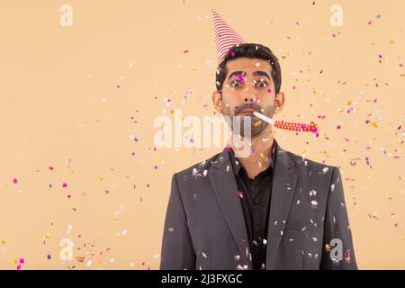 Happy business man in party hat blowing party horn while confetti falling on him Stock Photo