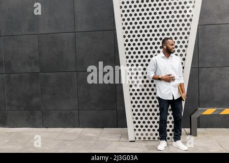 Concentrated stylish business guy wearing casual outfit, using smartphone, chatting with colleague. Handsome serious male freelancer standing outside Stock Photo