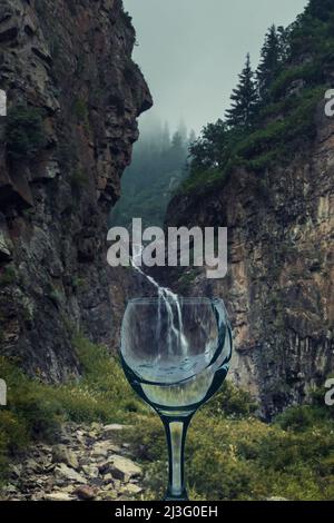 a transparent glass with clean and splashes of water on the background of mountain waterfall Stock Photo
