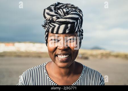Happy Muslim African woman wearing turban smiling in camera on the beach during summer vacation Stock Photo