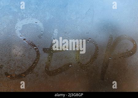 the word stop written on night wet window glass close-up with blurred background Stock Photo