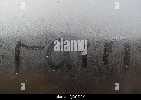 A word Rainy is written on the sweaty foggy window. Water droplets condensation background of dew on glass. Be happy even in bad rainy weather outside Stock Photo