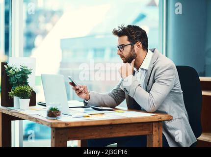 Another busy day at the office. Shot of a young businessman texting on his cellphone while working in an office. Stock Photo