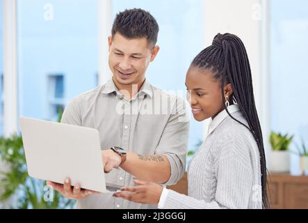 I think you have a strong idea here. Shot of two young businesspeople standing together in the office and using a laptop. Stock Photo