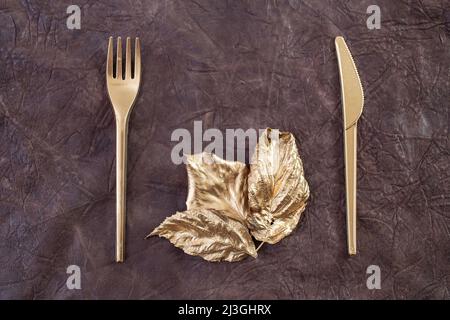 golden fork, knife and leaves, on brown leather texture, abstract wall art concept for food industry Stock Photo