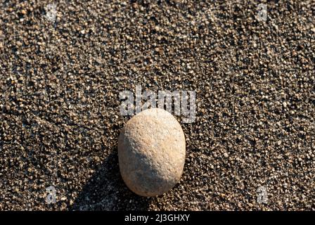 Small white stone isolated on dark gravel background in horizontal with sun Stock Photo