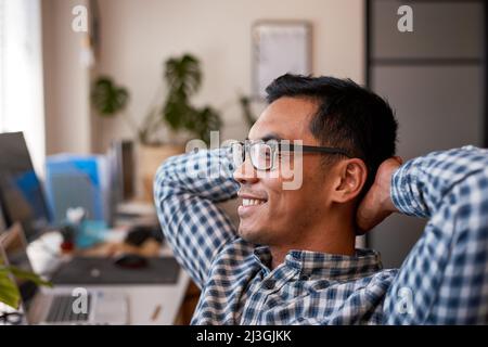 A young office worker leans back relaxing in his desk wearing spectacles Stock Photo