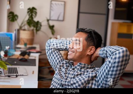 A young office worker leans back relaxing in his desk and smiles Stock Photo