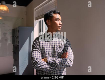 A businessman stands in the sunshine in office with arms crossed Stock Photo