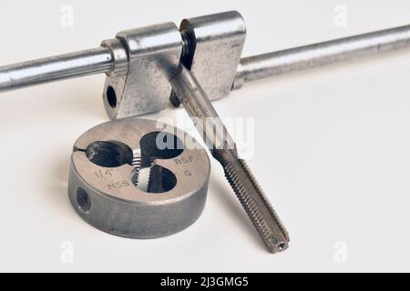 A metal thread cutting tap, held in an apprentice hand made Tap Holder, with a thread cutting die beside it.1/4' BSF thread. England, UK Stock Photo