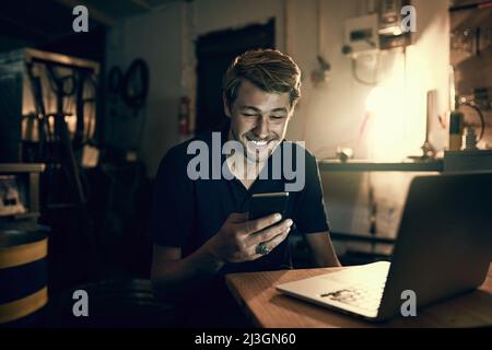 Staying connected and up to date. Cropped shot of a handsome young man sending a text while working late in his office. Stock Photo