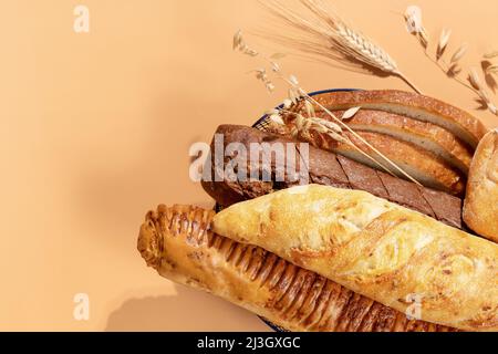 Homemade natural breads. Fresh loafs of bread in the blue basket with ears of rye and wheat on a beige background with copy space. Crunchy french bagu Stock Photo