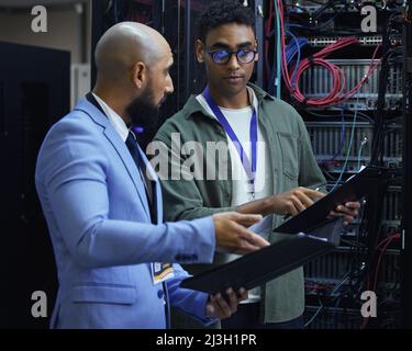 Going over the diagnostic report. Cropped shot of two male IT support agents working together in a dark network server room. Stock Photo