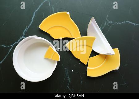 Top view of broken white and yellow pottery scattered on black floor Stock Photo