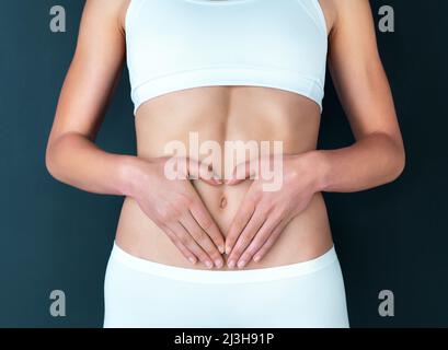 For the greatest wealth, invest in your health. Studio shot of a fit young woman making a heart shaped gesture over her stomach against a dark Stock Photo