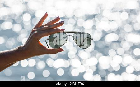 Sunglasses in a woman hand against blurred background with bokeh reflections Stock Photo