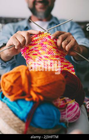 Close up of adult man working with ball yarn of colorful wool. Happy people in indor hobbies activity using woolen and doing knitting work. Indoor leisure activity Stock Photo