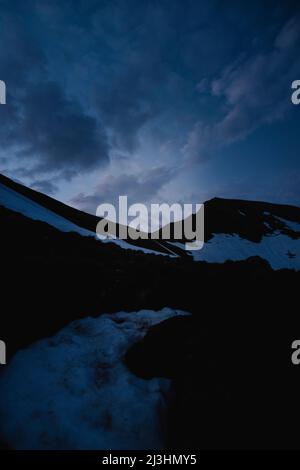 moon peaking between mountains during sunrise in snowy and mountainous landscape Stock Photo