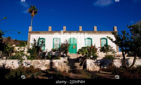 Canary Islands, Lanzarote, volcanic island, north of the island, oasis town, Haria, flat building with green doors and windows, garden in front, palm trees, sky blue Stock Photo
